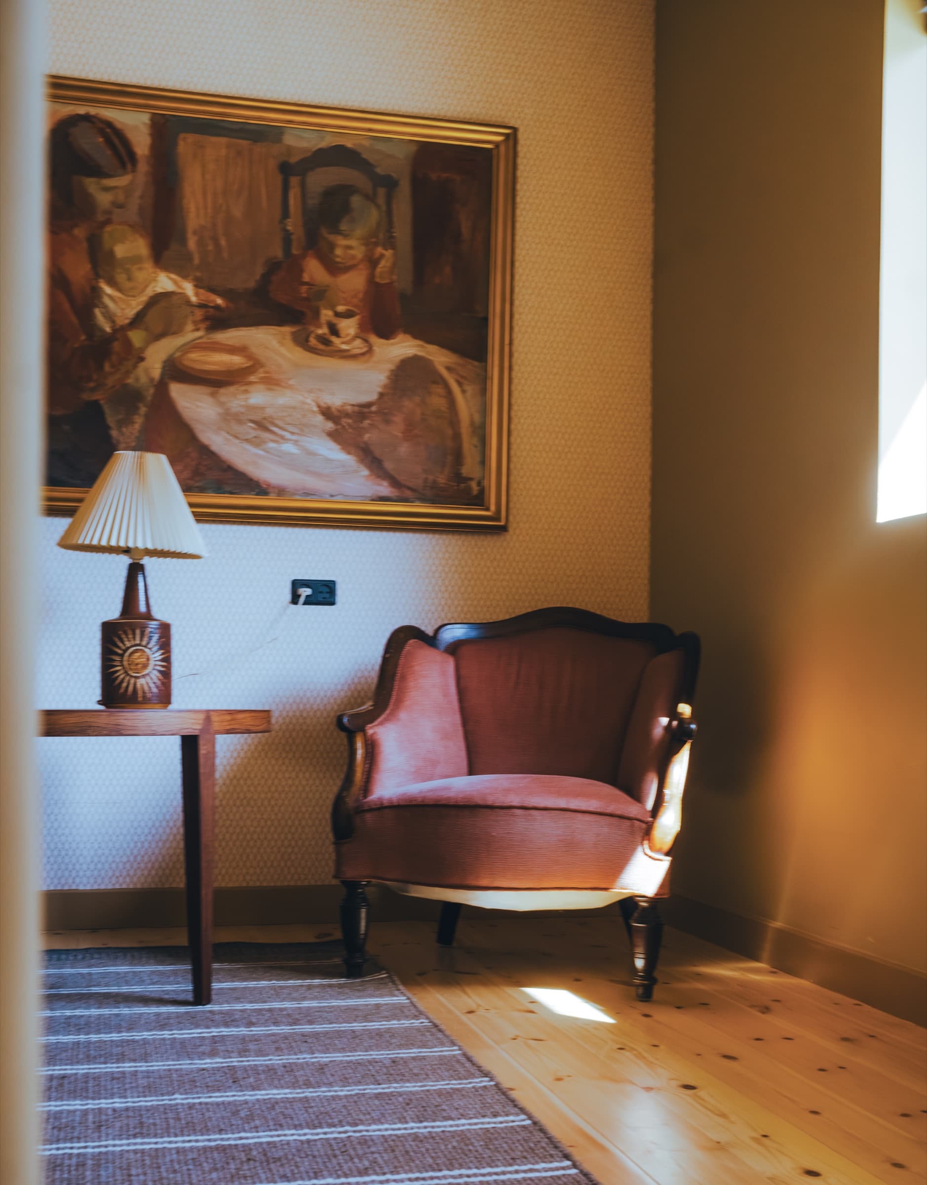 Historisk stuehjørne på Store Lærkegård med antik lænestol i rosa velour, indrammet maleri og keramiklampe i det varme lys